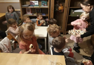 Dzieci siedzą przy stolikach, częstują się ciasteczkami.